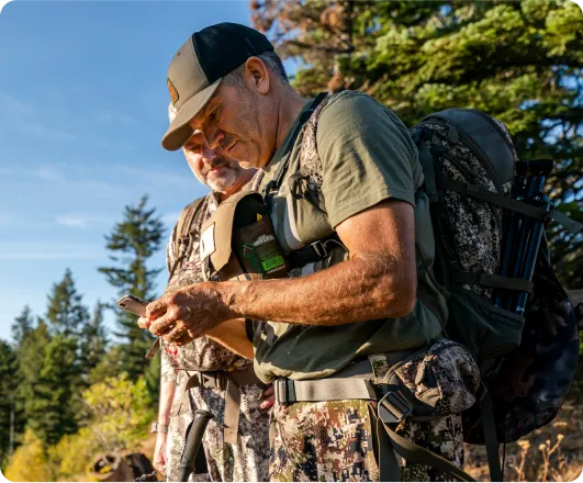 Two hunters using the MNDNR licensing system on a mobile phone while out in the wilderness.